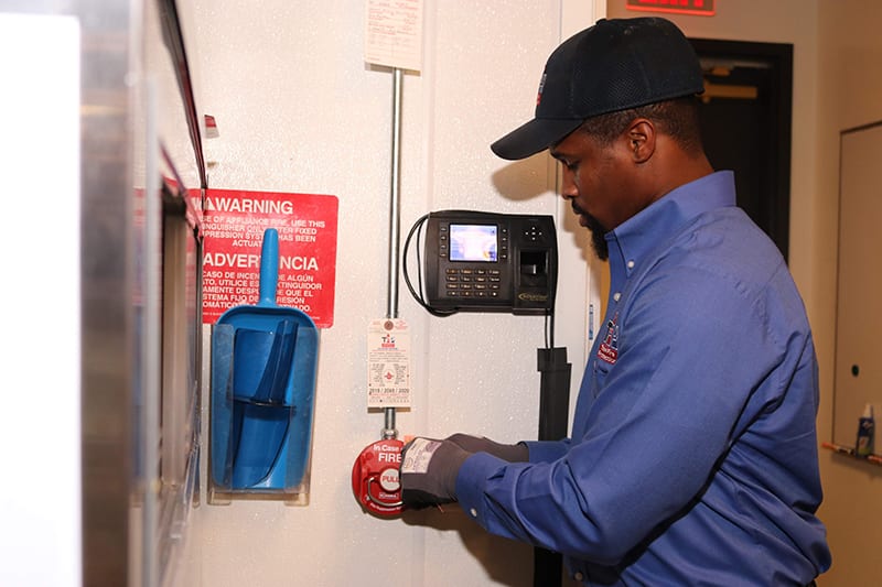 Total Fire Protection technician inspecting kitchen fire suppression system.